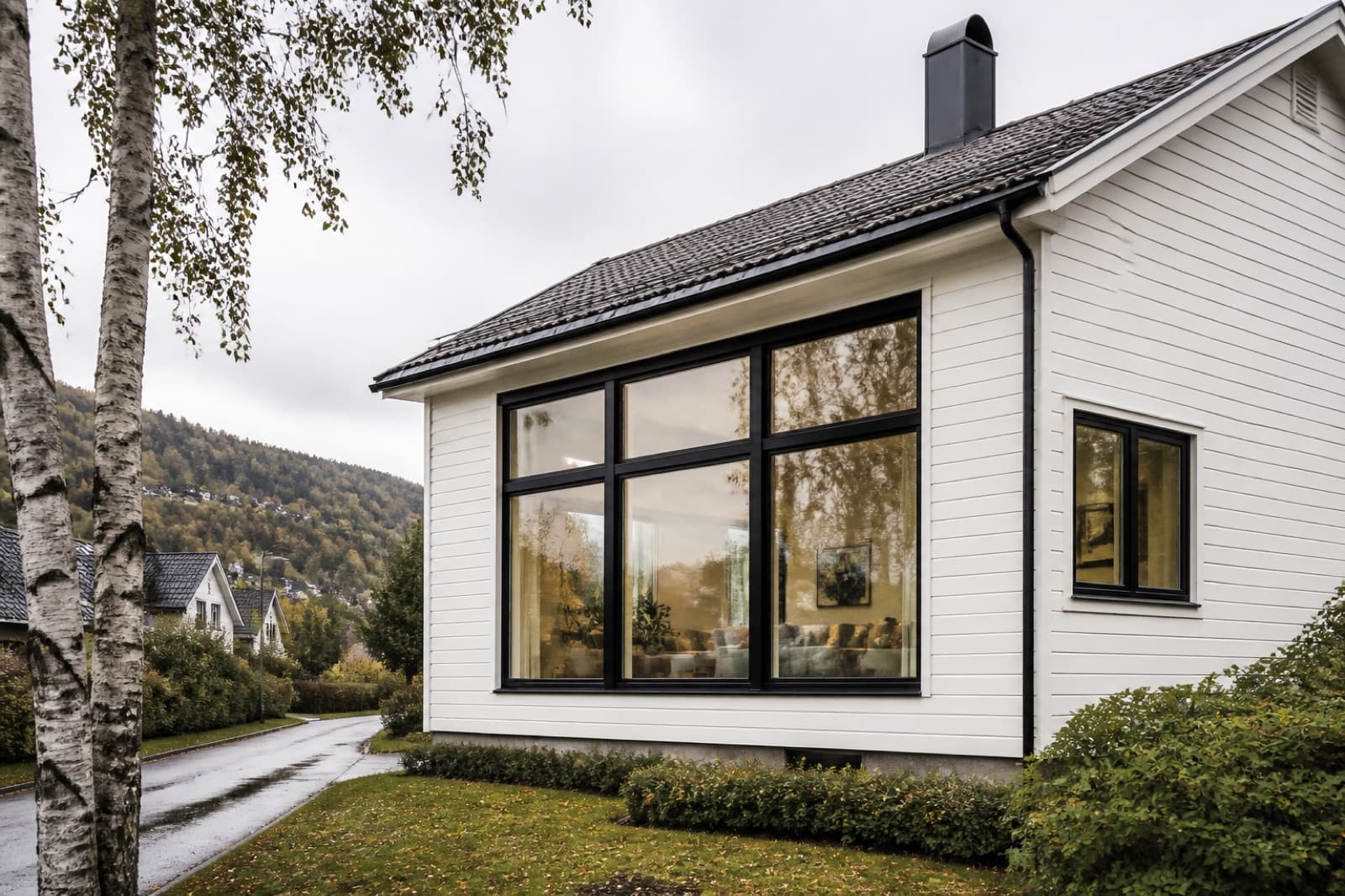 Hvit enebolig med store, mørke vinduer i fasaden